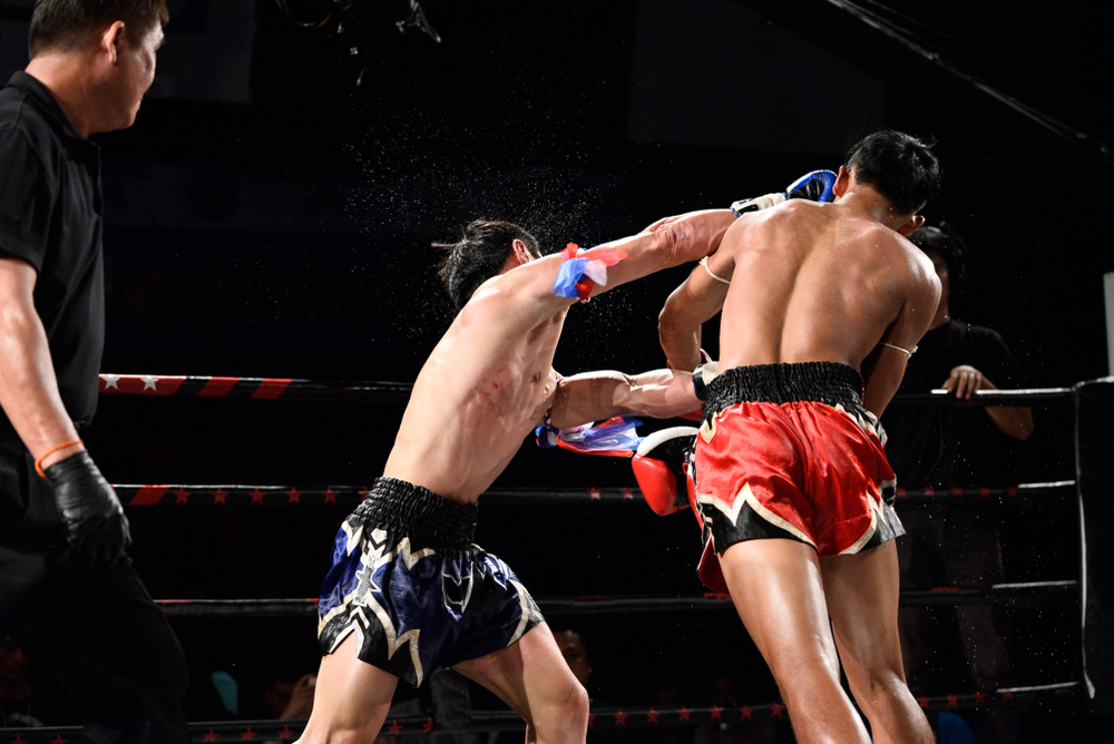 Two fighters during a Muay Thai fight Bangkok stadium card in the evening.